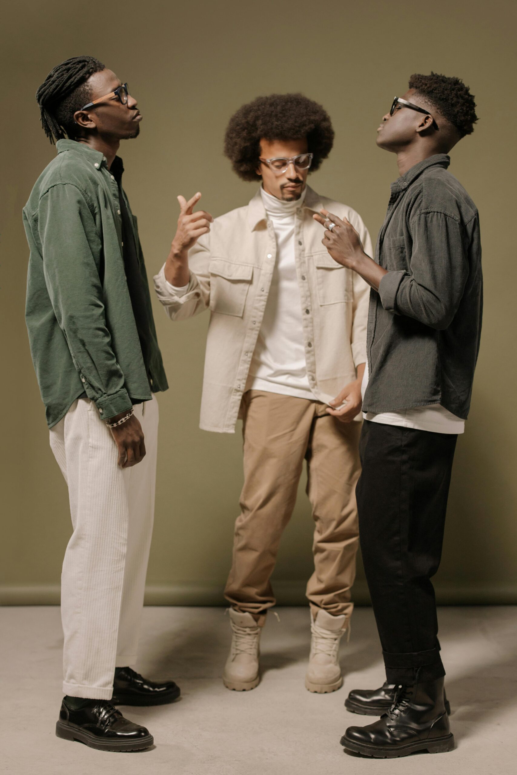 Three men in trendy outfits pose confidently on a neutral backdrop, showcasing modern fashion.